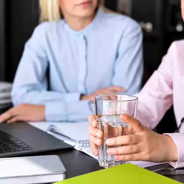 Employee holding a glass of water during a workplace discussion with a colleague